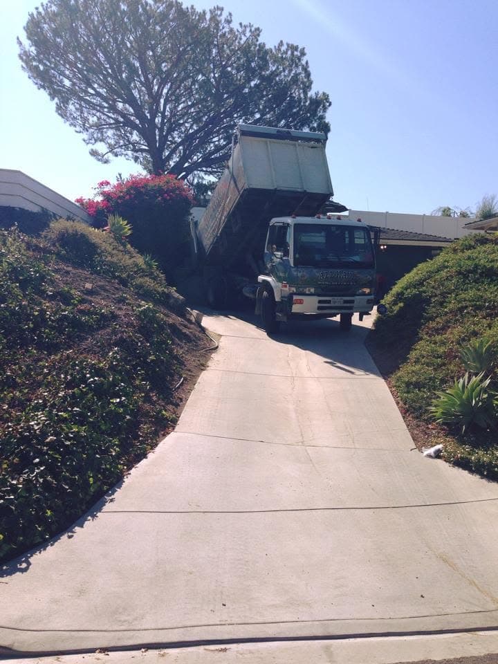 All Haul truck bed tilted, dumping debris into a driveway
